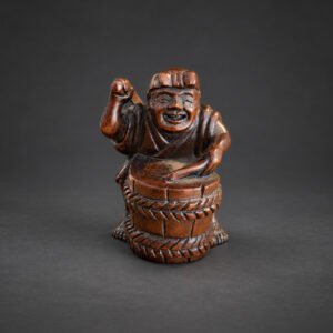Late 19th-century Japanese wood netsuke of a jovial drummer performing at a barrel-shaped drum, signed 友正 Tomomasa.