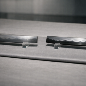 Wide editorial close-up comparing sashikomi and hadori polishes: two Japanese sword blade sections side by side on a neutral silk mat under raking museum light, left subtly natural hamon, right brighter hadori band, with no markings or text.