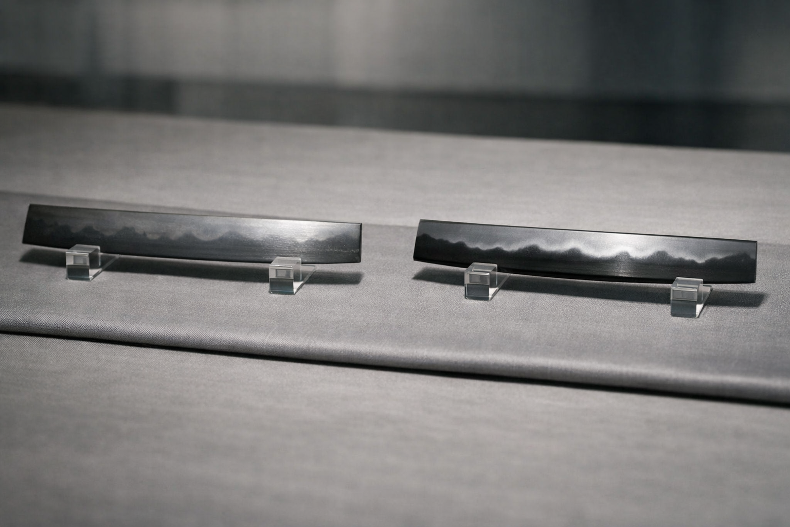 Wide editorial close-up comparing sashikomi and hadori polishes: two Japanese sword blade sections side by side on a neutral silk mat under raking museum light, left subtly natural hamon, right brighter hadori band, with no markings or text.