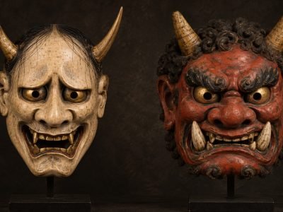 Ilustración de una máscara Hannya pálida junto a una máscara Oni roja, destacando el contraste entre sus rasgos faciales.