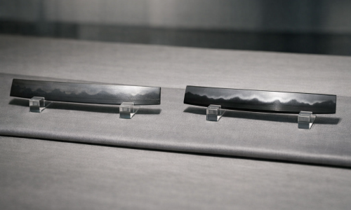 Wide editorial close-up comparing sashikomi and hadori polishes: two Japanese sword blade sections side by side on a neutral silk mat under raking museum light, left subtly natural hamon, right brighter hadori band, with no markings or text.